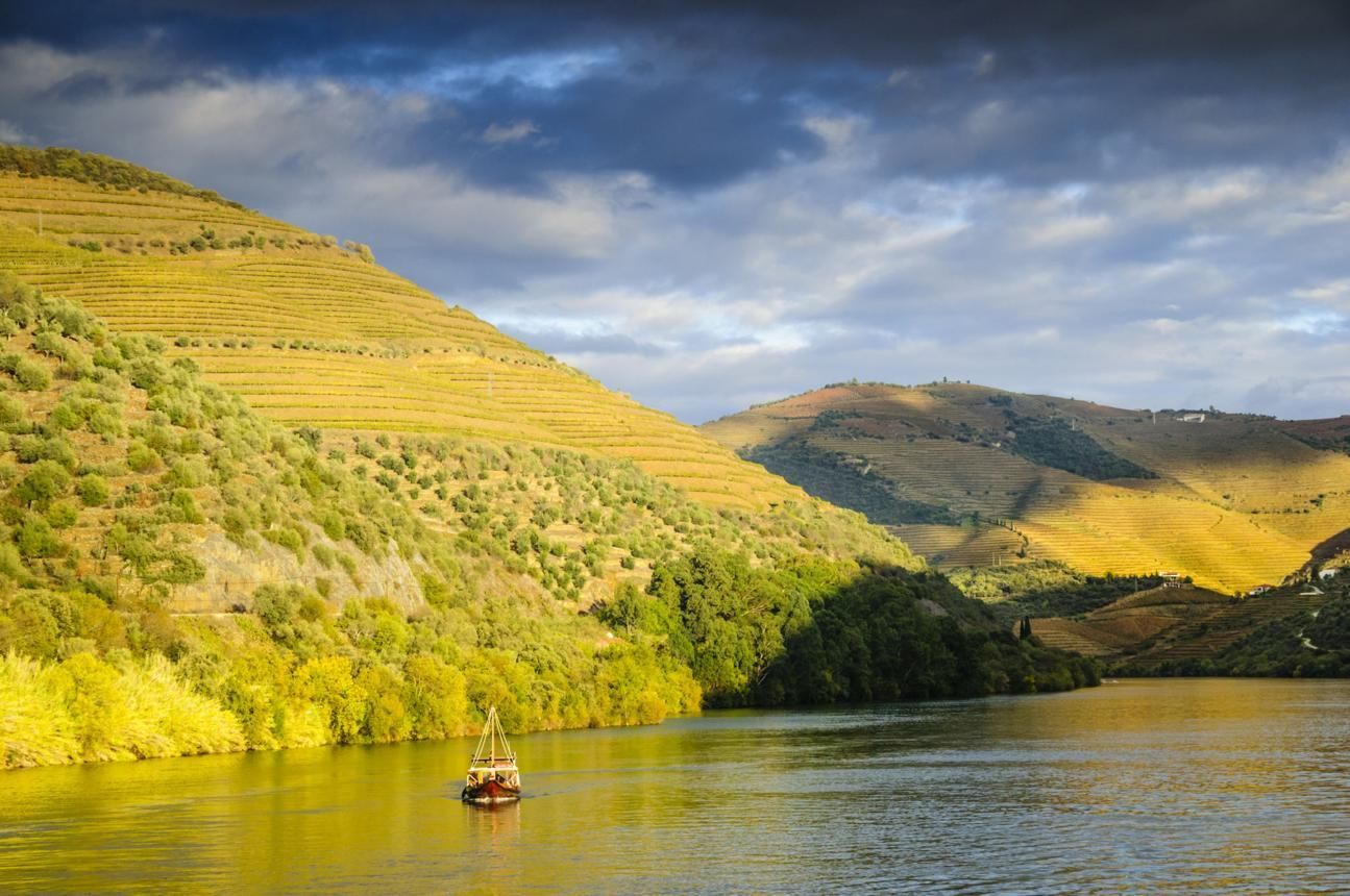 Sunlit river with a small boat, green hills, and cloudy sky reflecting on the water