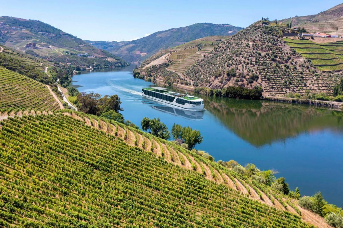 River cruise ship on a blue river between terraced green hills and vineyards under a clear sky