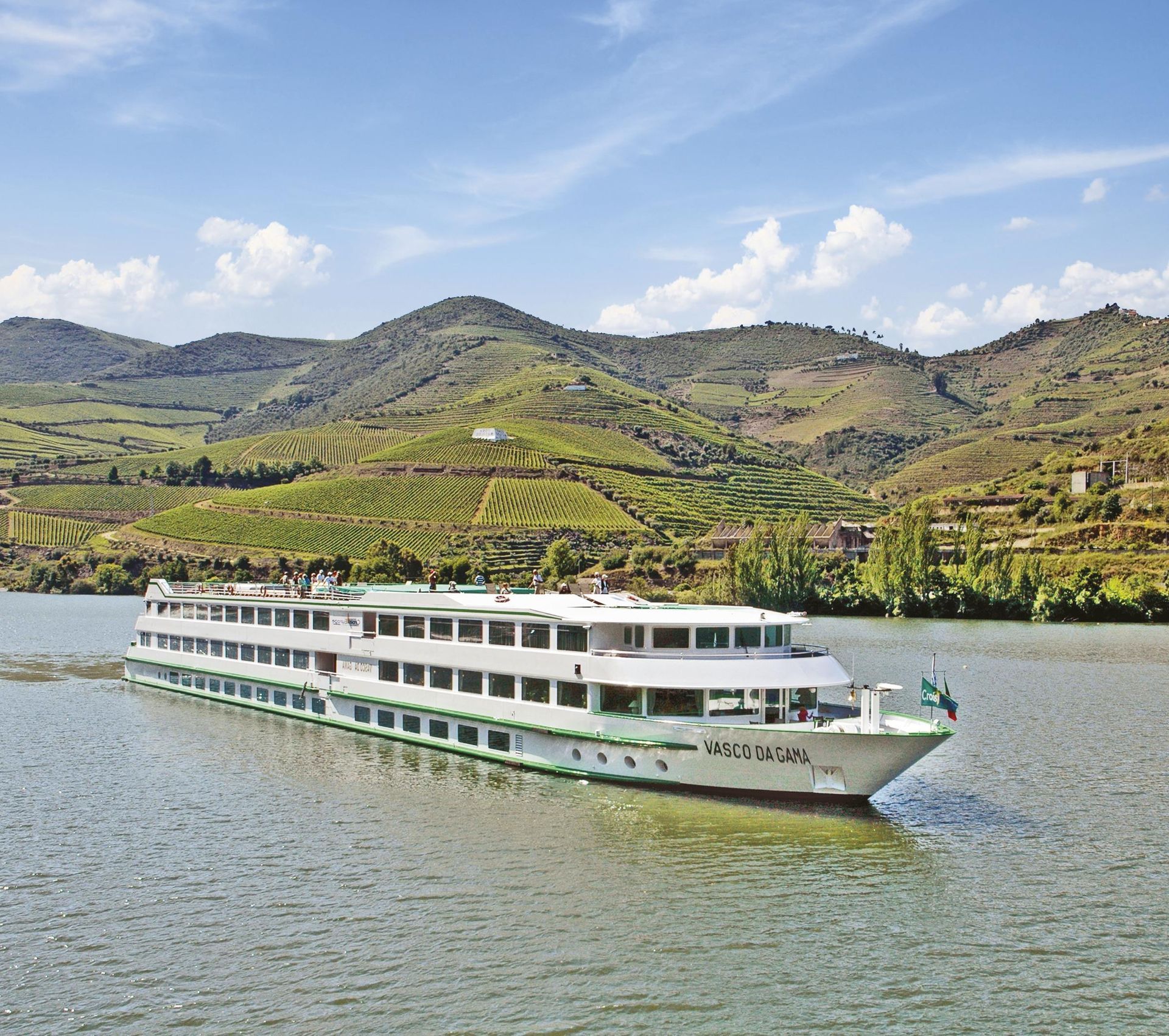 White river cruise boat on calm water with green terraced hills and a partly cloudy sky