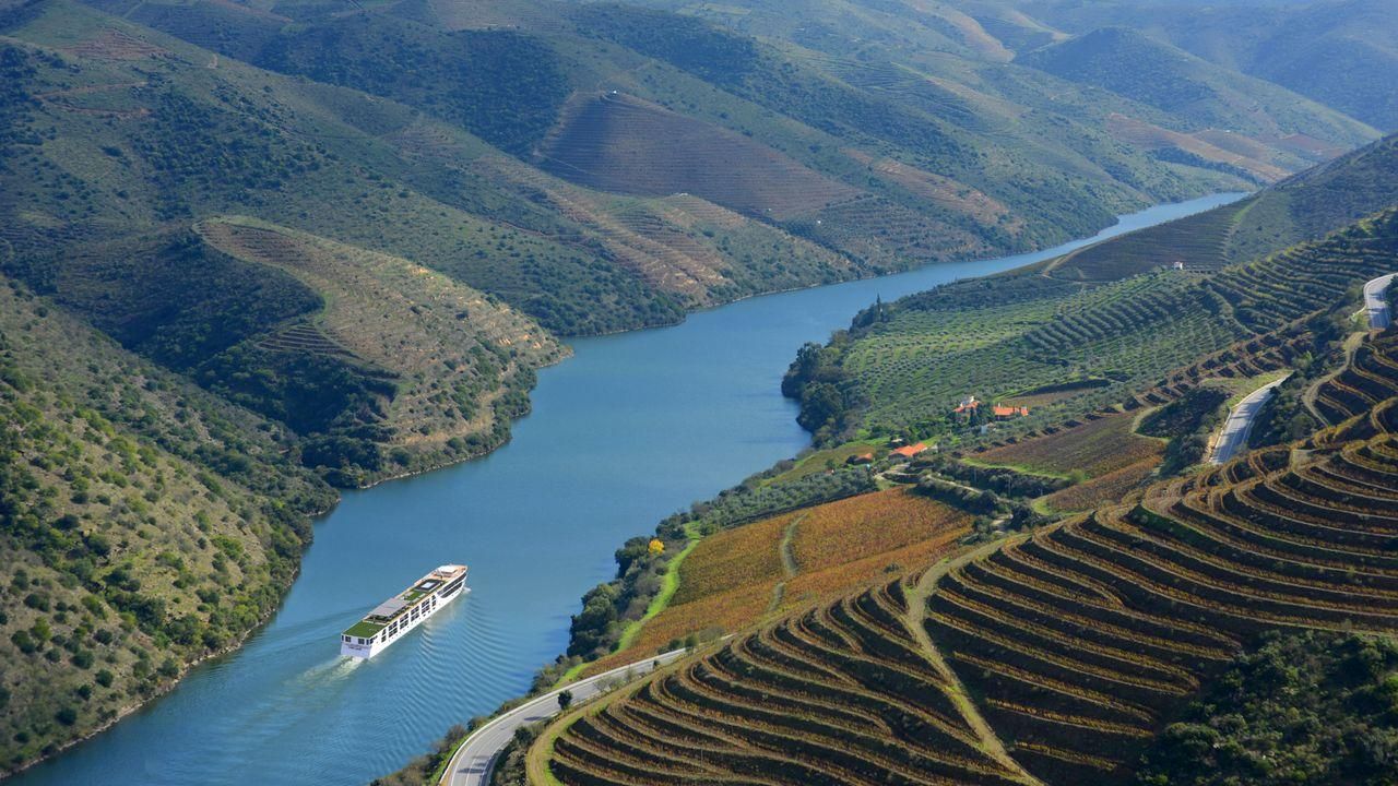 River cruise ship on a winding blue river through green terraced hillsides and vineyards