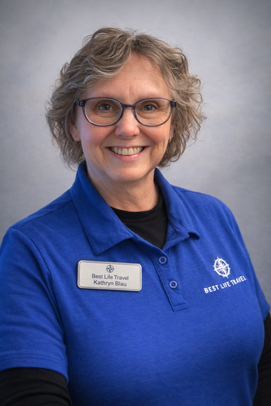 A person smiling while wearing a blue polo shirt with a logo and a name tag against a grey background.