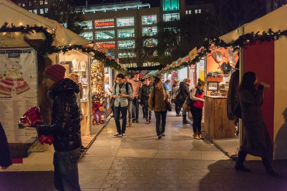 People walking through a festive market street lined with lit wooden stalls at night