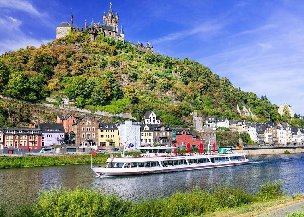 Riverboat on a river with a hillside town and castle on the hill under a bright blue sky
