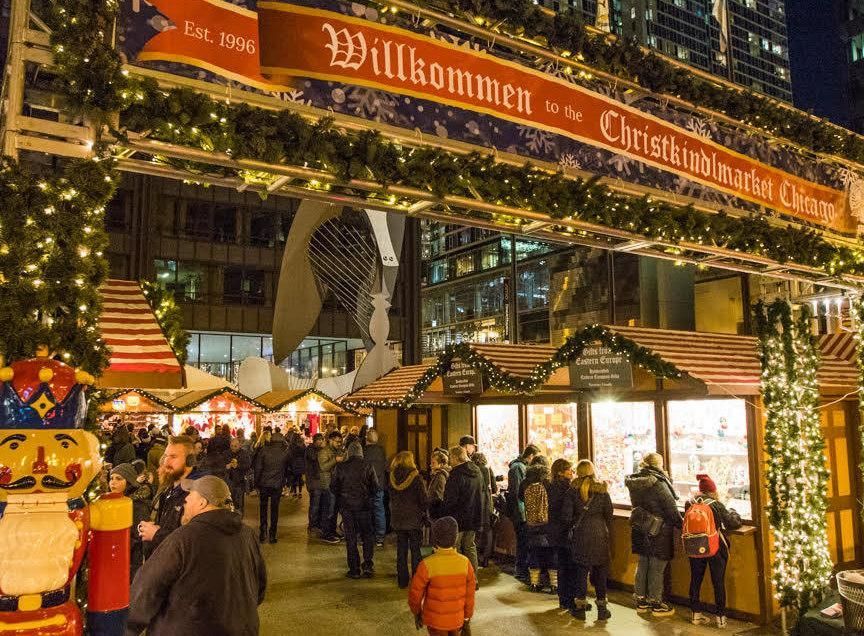 Festive Christmas market entrance lit with warm lights and crowds under a “Willkommen” banner