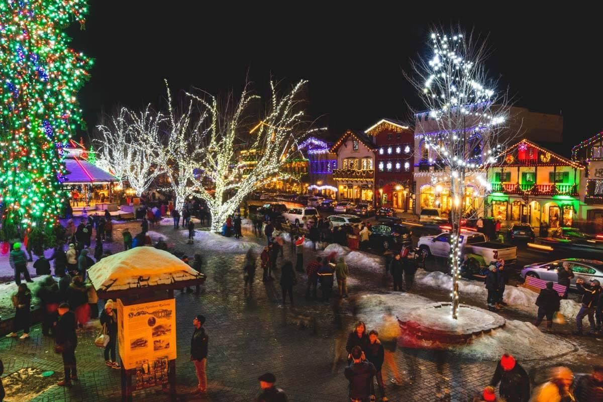 Snowy night market with colorful holiday lights, decorated trees, and crowds in a festive square