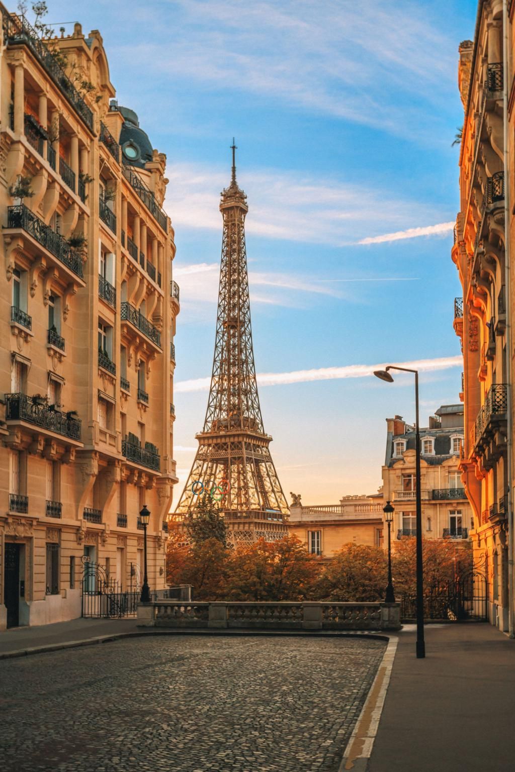 Eiffel Tower framed by Parisian buildings on a cobblestone street at sunset