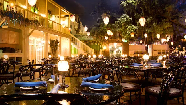 Outdoor restaurant dining area at night, illuminated by numerous hanging lanterns and table lamps.