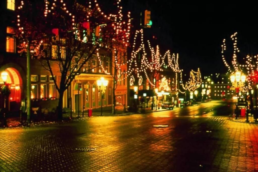Nighttime city street with festive lights, wet pavement, and warmly lit storefronts