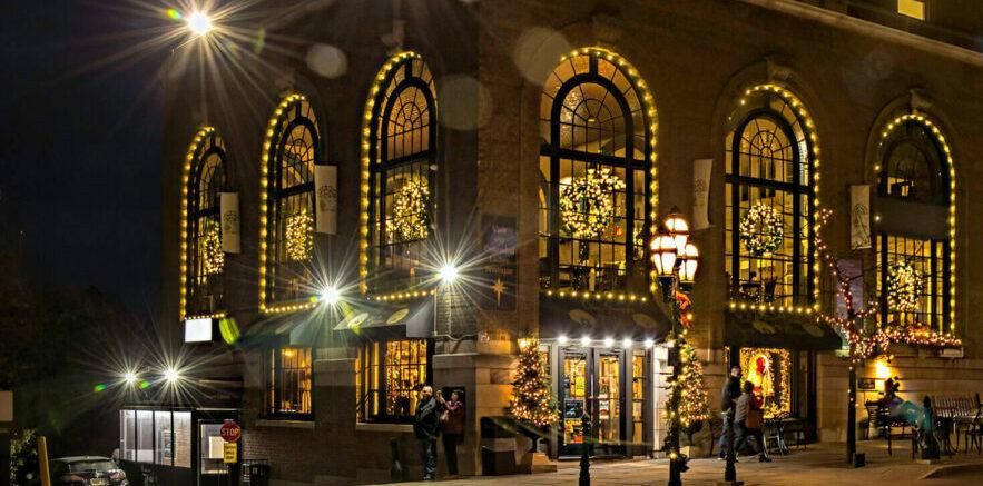 Nighttime view of a brightly lit building with arched windows and festive string lights on the corner.
