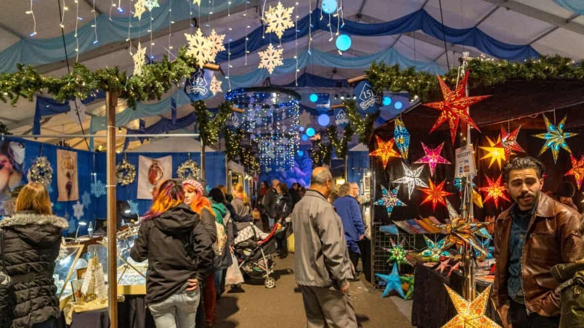 Festive outdoor market stall with glowing star lanterns and shoppers under a blue canopy