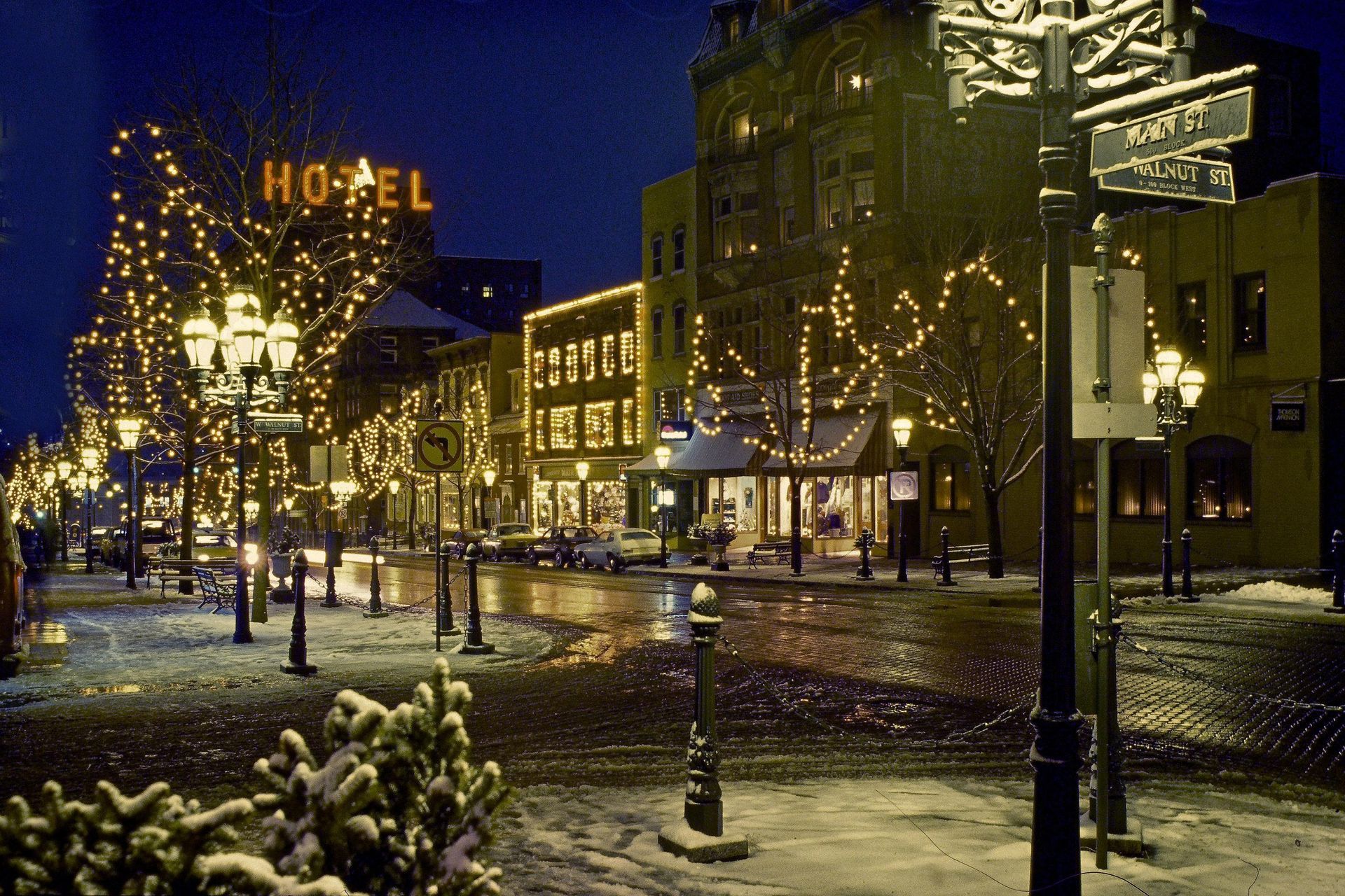 Snowy nighttime hotel plaza with lit lampposts and holiday lights