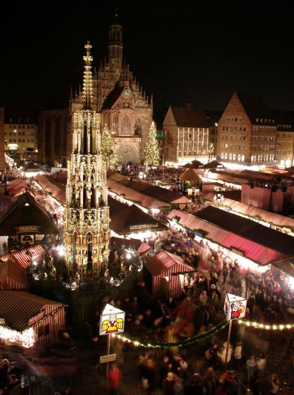 Nighttime Christmas market with lit stalls and a tall illuminated cathedral tower in the background