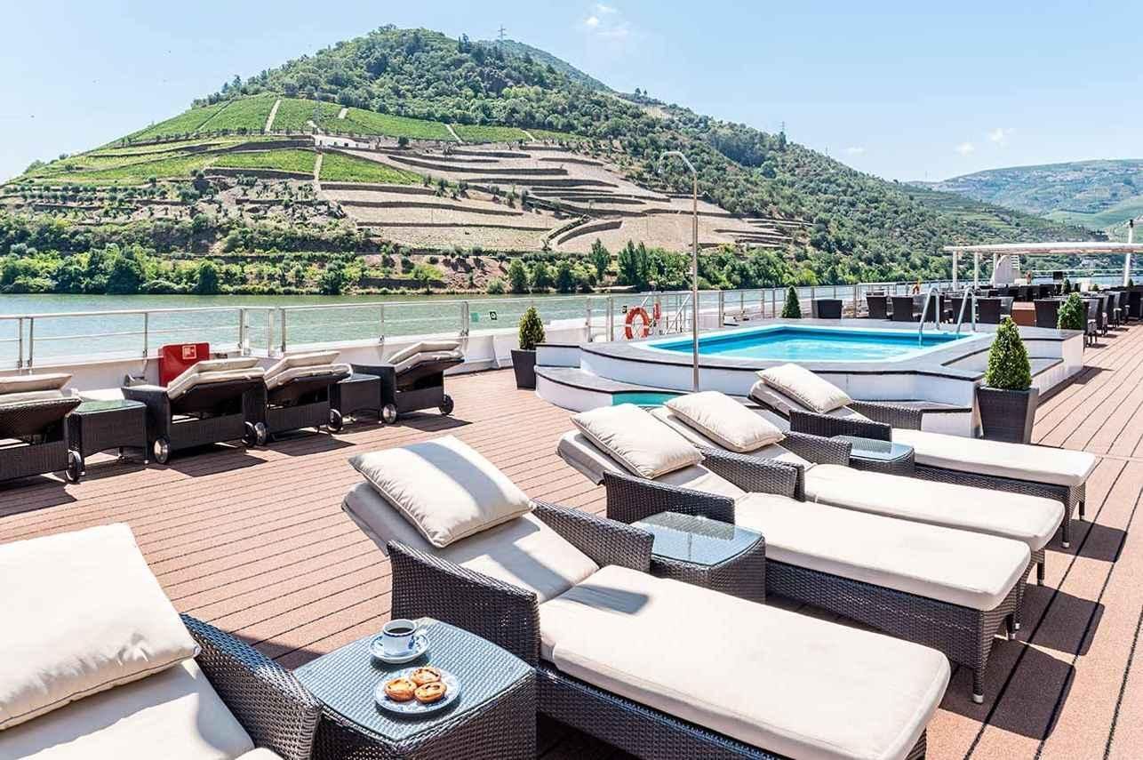 Poolside lounge chairs overlooking a terraced green hillside under a bright sky