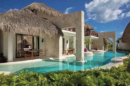 Luxury tropical resort suites with thatched roofs, stone walls, and private pool access under a clear blue sky.