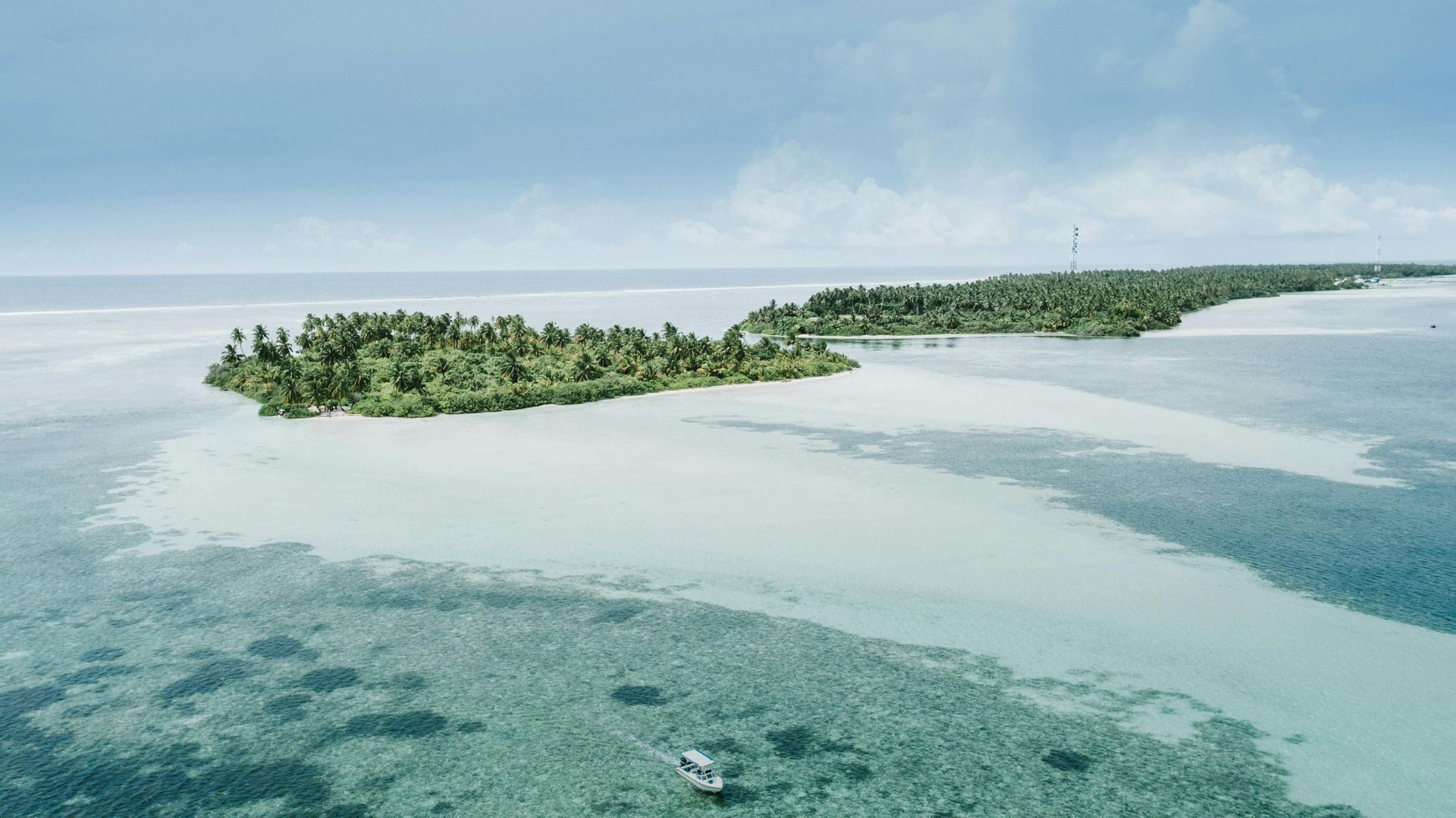Aerial view of a lush green tropical island surrounded by shallow turquoise water and a small boat in the foreground.