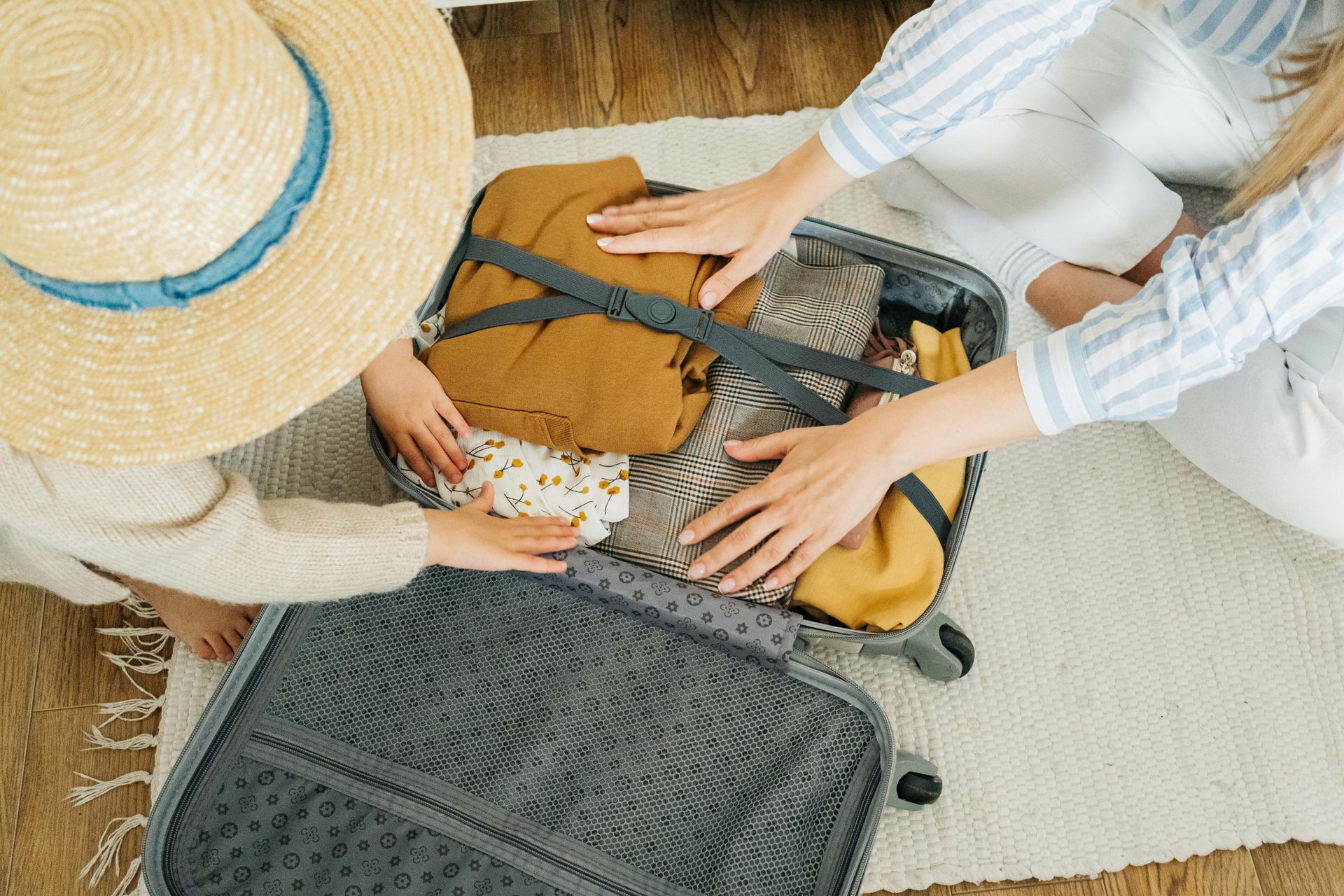 Two women are sitting on the floor packing a suitcase.