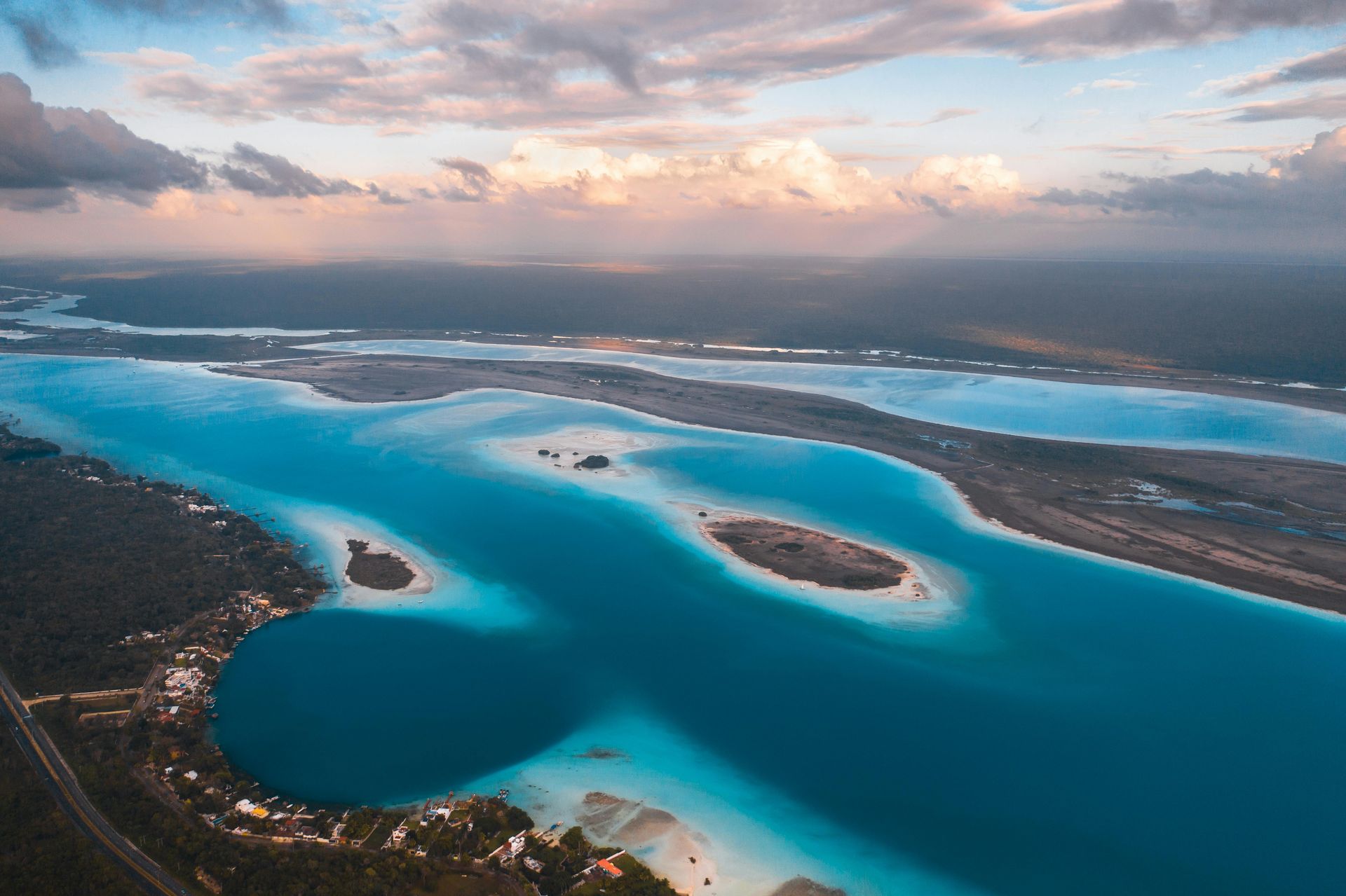 Aerial view of the turquoise waters and small islands of Laguna Bacalar in Mexico under a cloudy sunset sky.