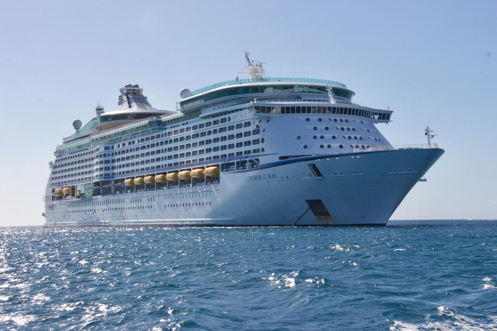A large white Royal Caribbean cruise ship sailing on bright blue, sun-dappled water under a clear sky.