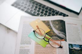 Eyeglasses on an open magazine beside sticky notes and a laptop keyboard