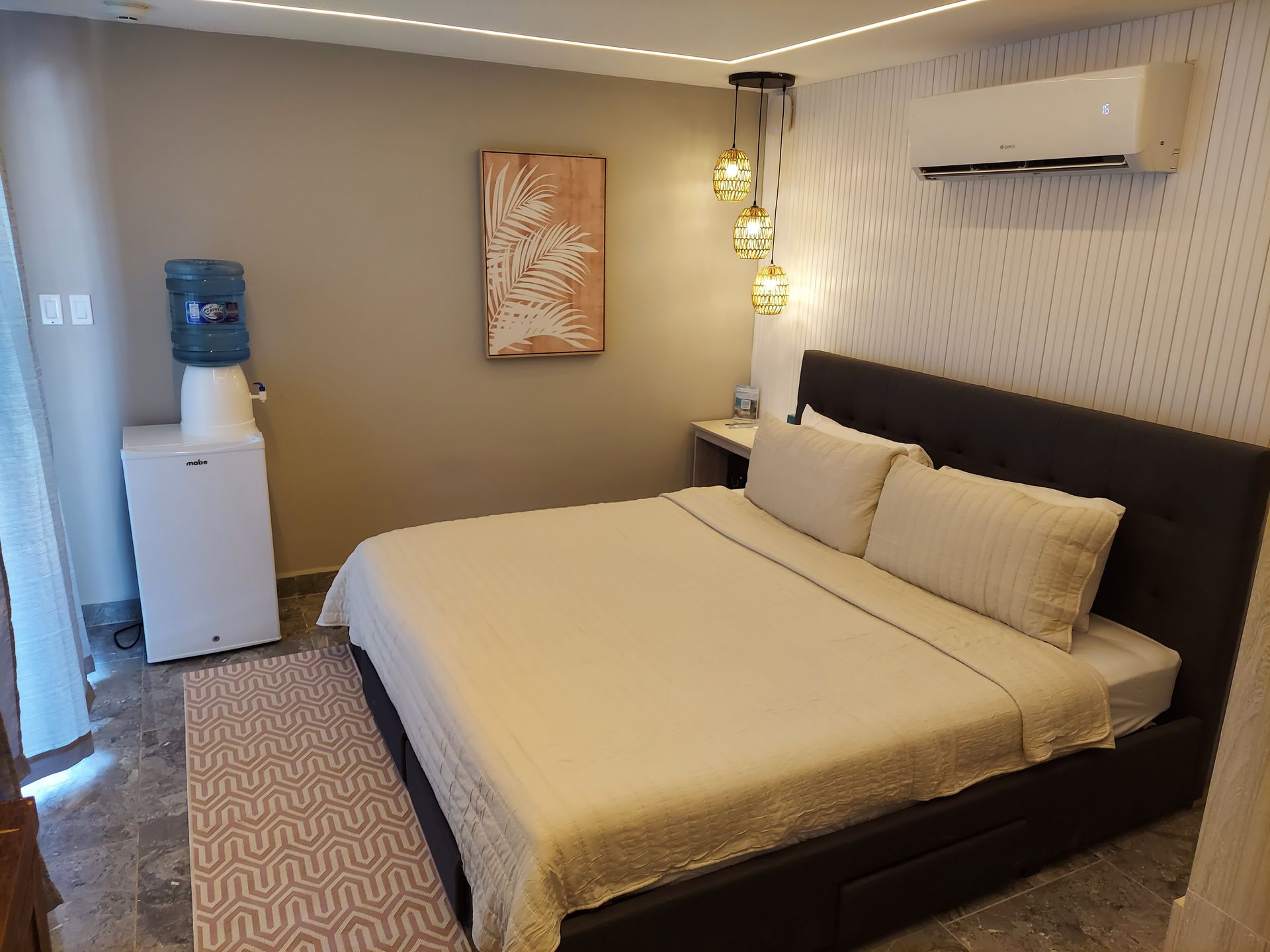 Modern hotel room with a king bed, wall art, water dispenser, and air conditioner