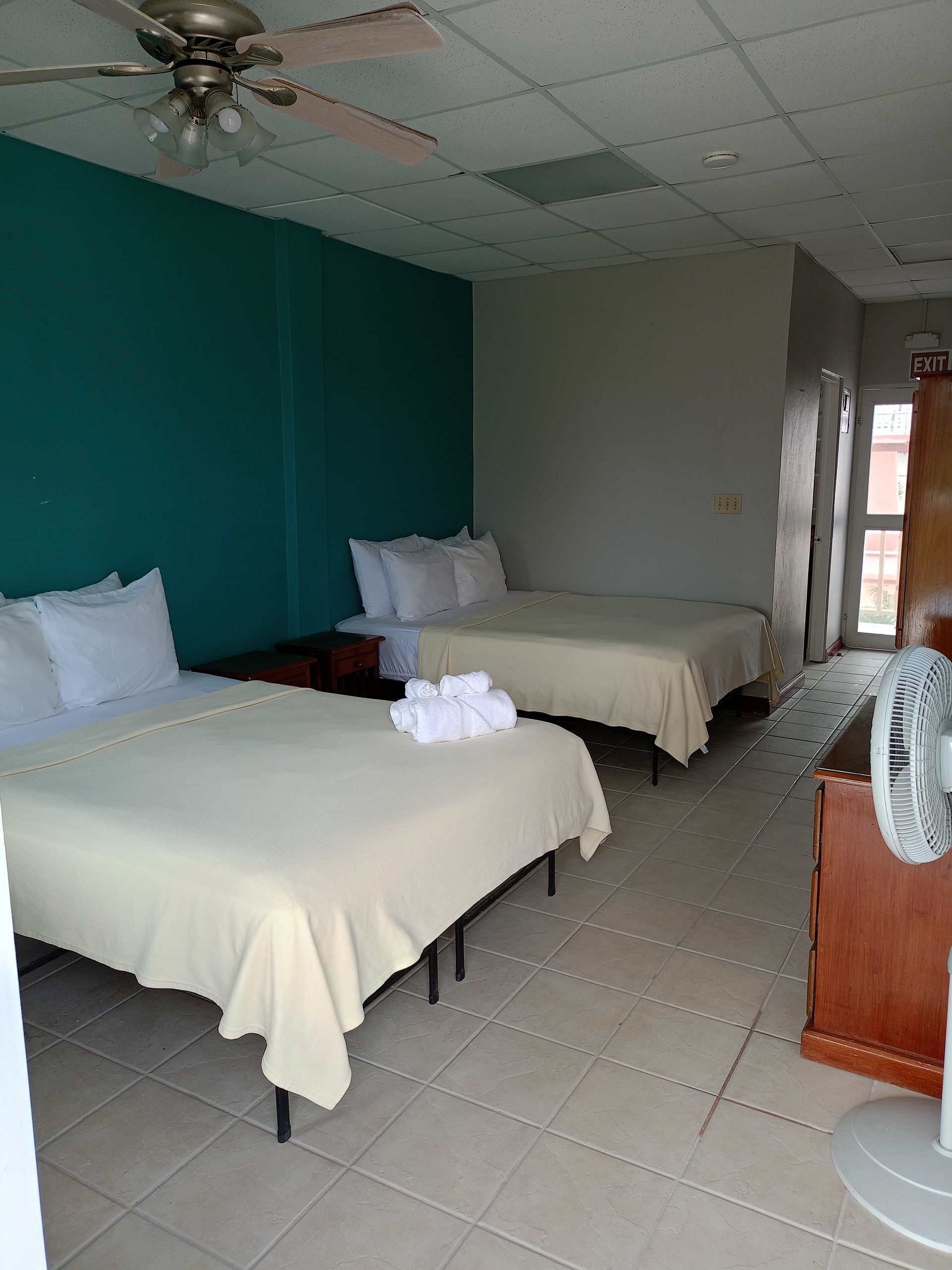 Hotel room with two double beds, teal wall, and a fan.