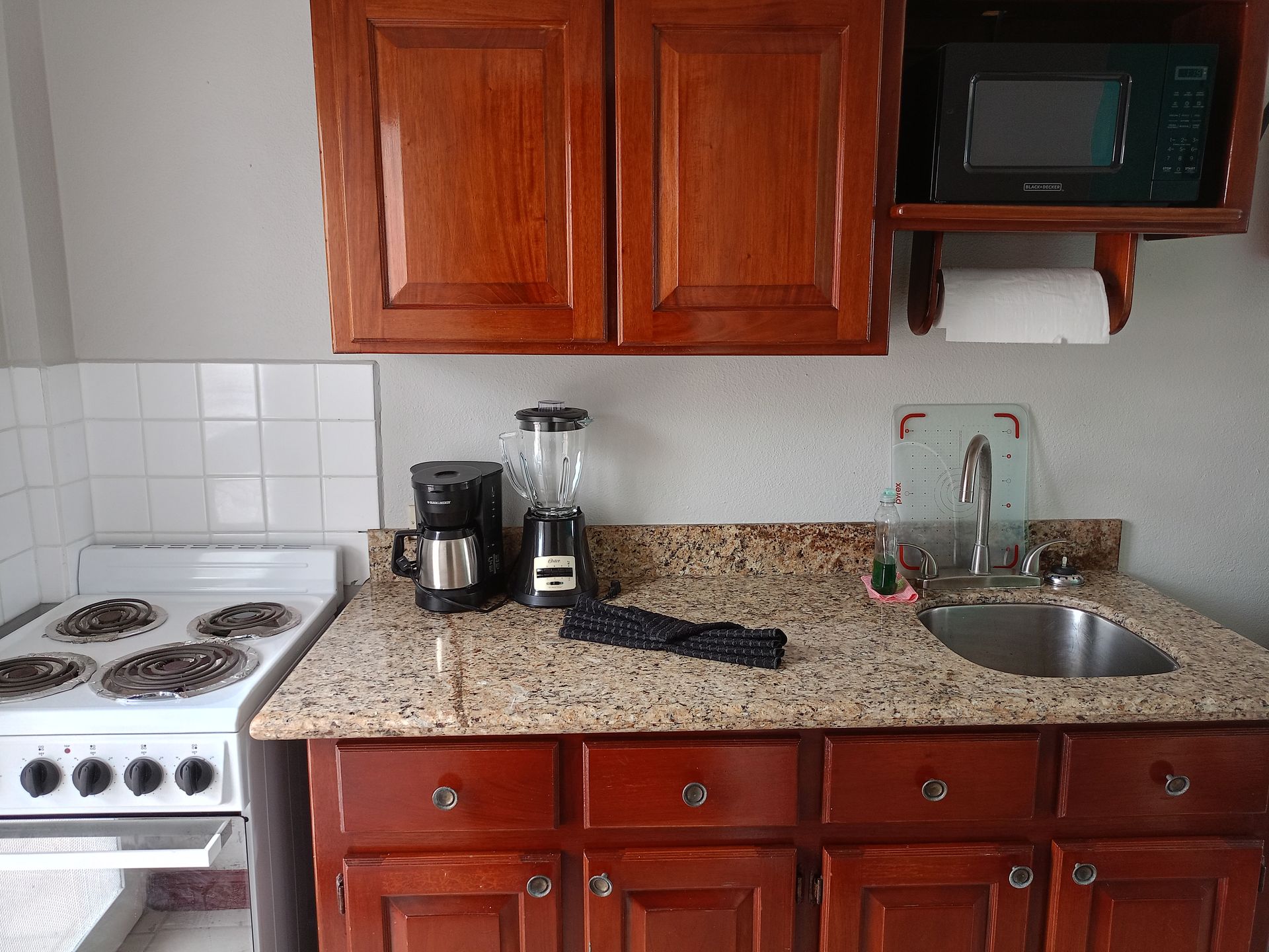 Kitchen with brown cabinets, white stove, granite countertop, and microwave.