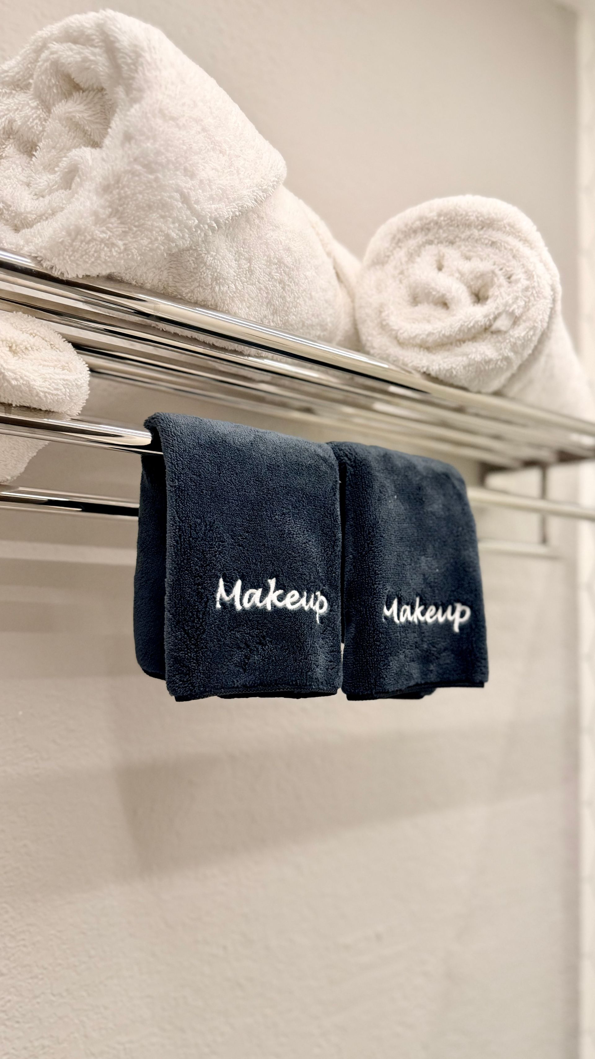 White towels on a wire shelf with two dark blue “Makeup” towels hanging below.