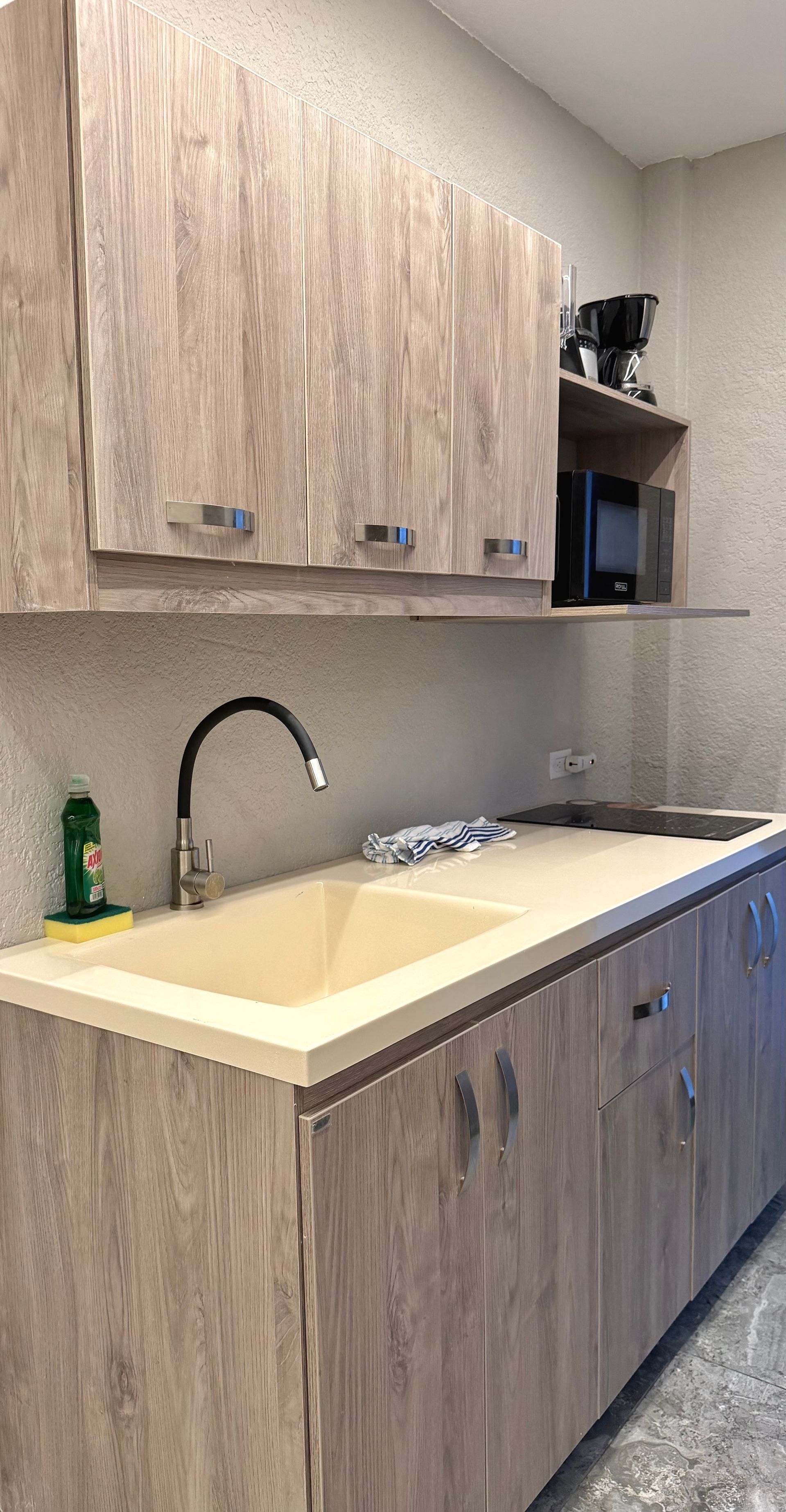 Small kitchenette with wood cabinets, cream sink, faucet, and countertop in a modern office break area