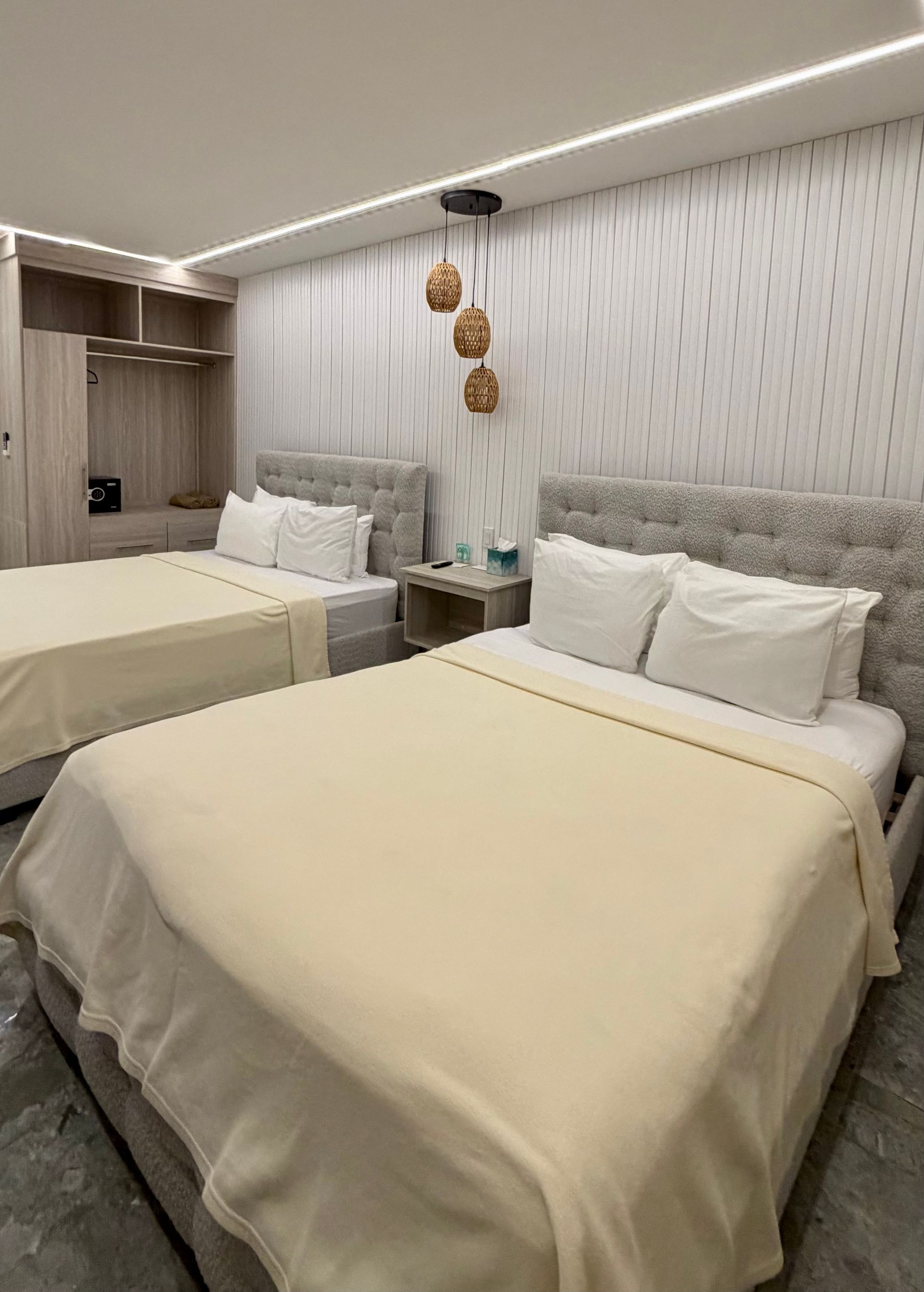 Small hotel room with two neatly made twin beds, white bedding, and soft gray decor