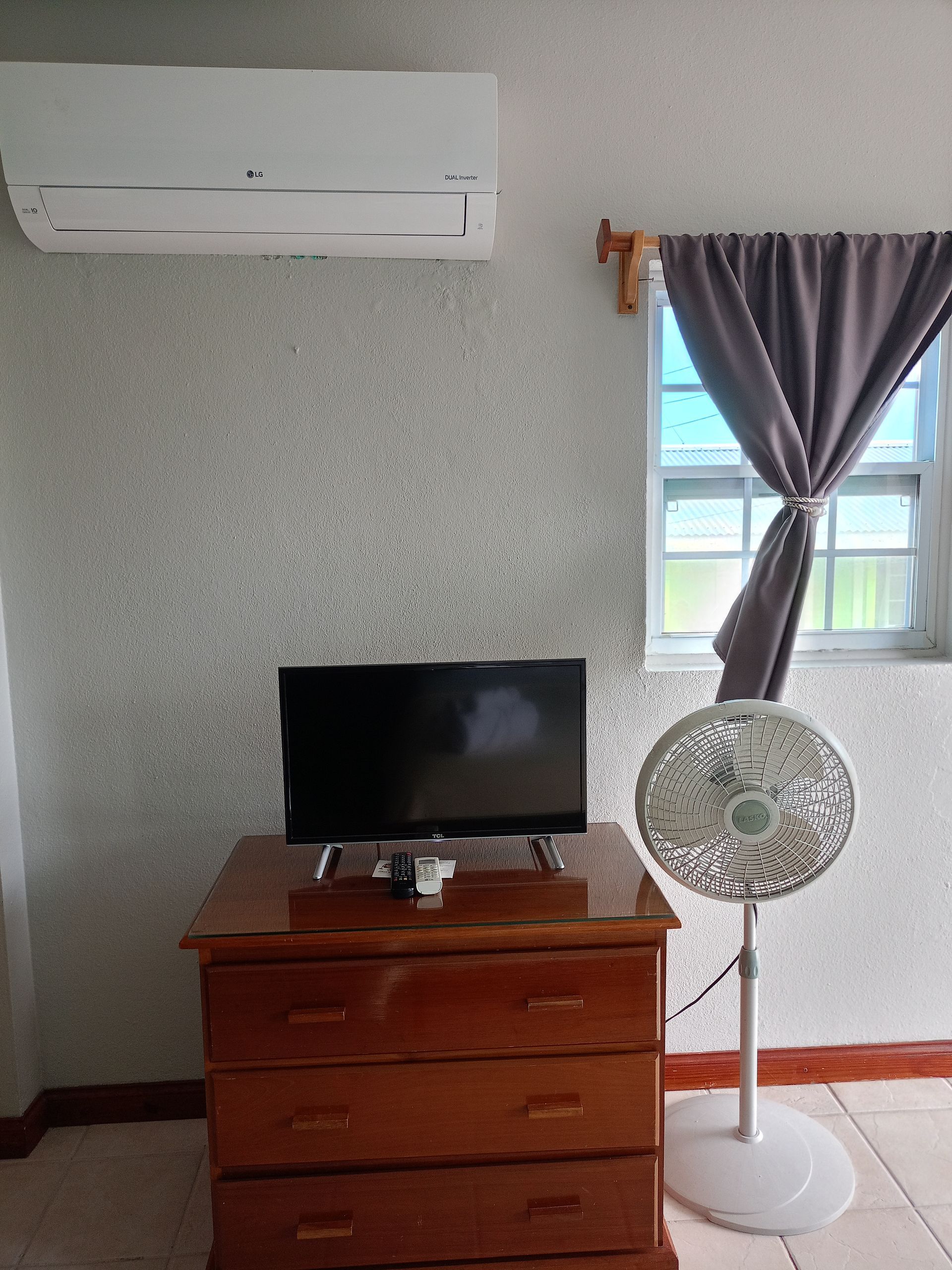 A room with a TV on a wooden dresser, a fan, and an air conditioner unit mounted on the wall.