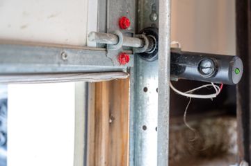 Close-up of a metal garage door hinge with red rollers and a black latch.