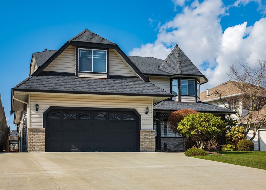 Suburban two-story house with black garage doors, beige siding, and a stone entry under a blue sky.