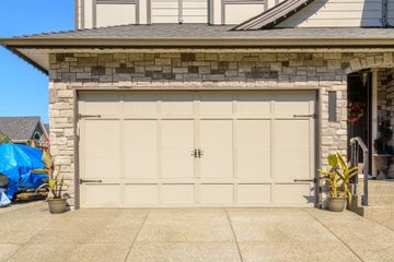 Beige two-car garage door on a stone-faced suburban house, with potted plants at the entrance