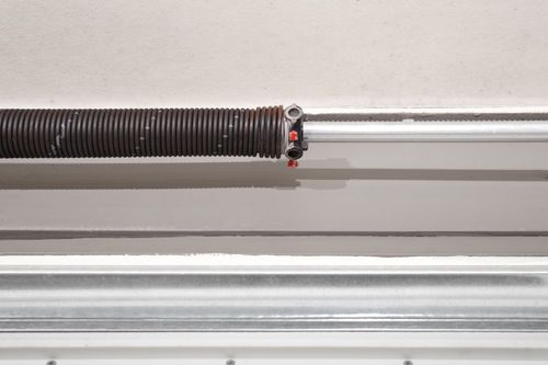 Close-up of a garage door torsion spring and metal track with red cable hardware