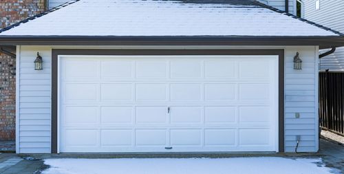 White two-car garage with closed door and light snow on the roof and ground