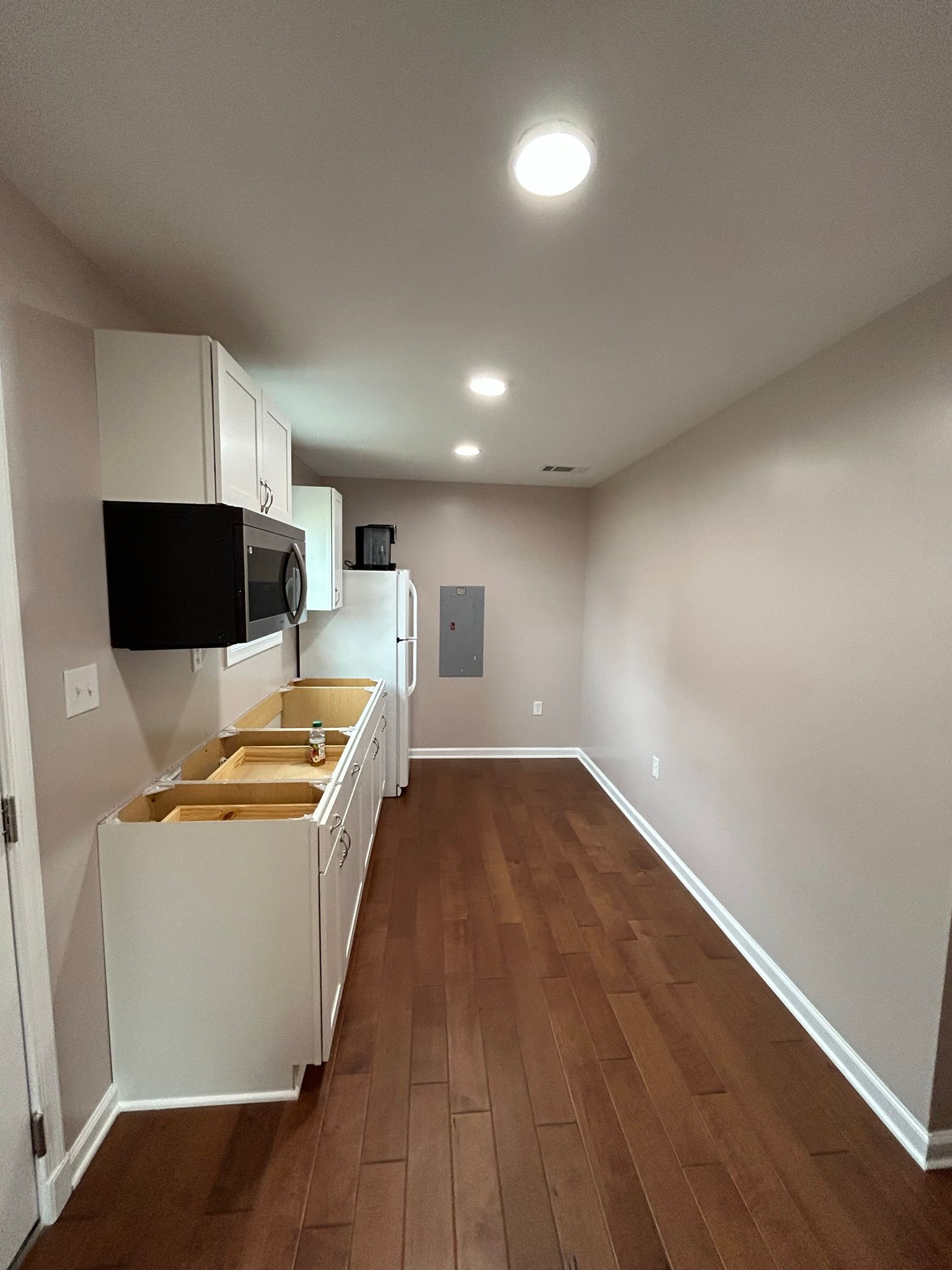 A long kitchen with hardwood floors and white cabinets.