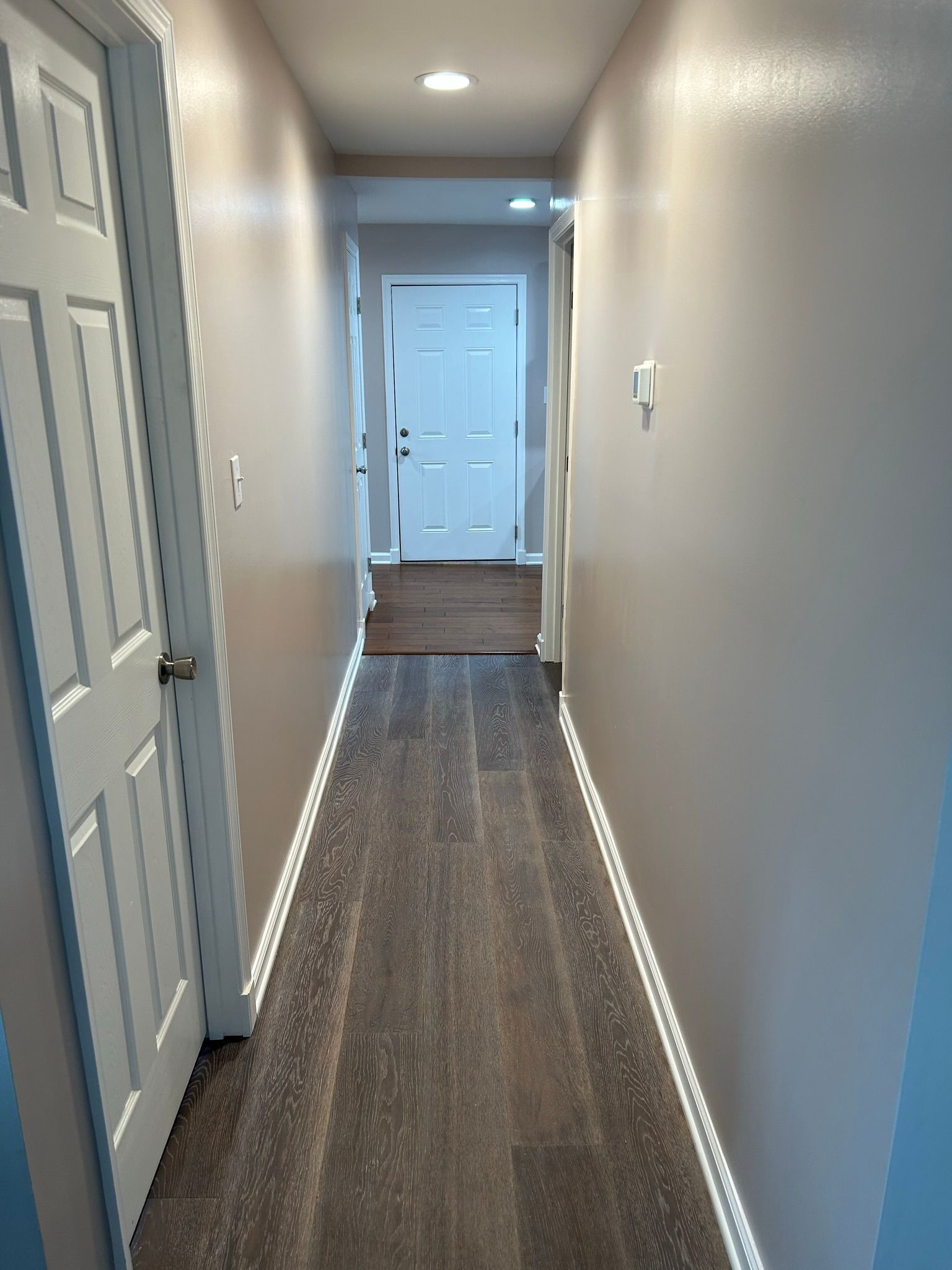 A long hallway with hardwood floors and white walls leading to a door.