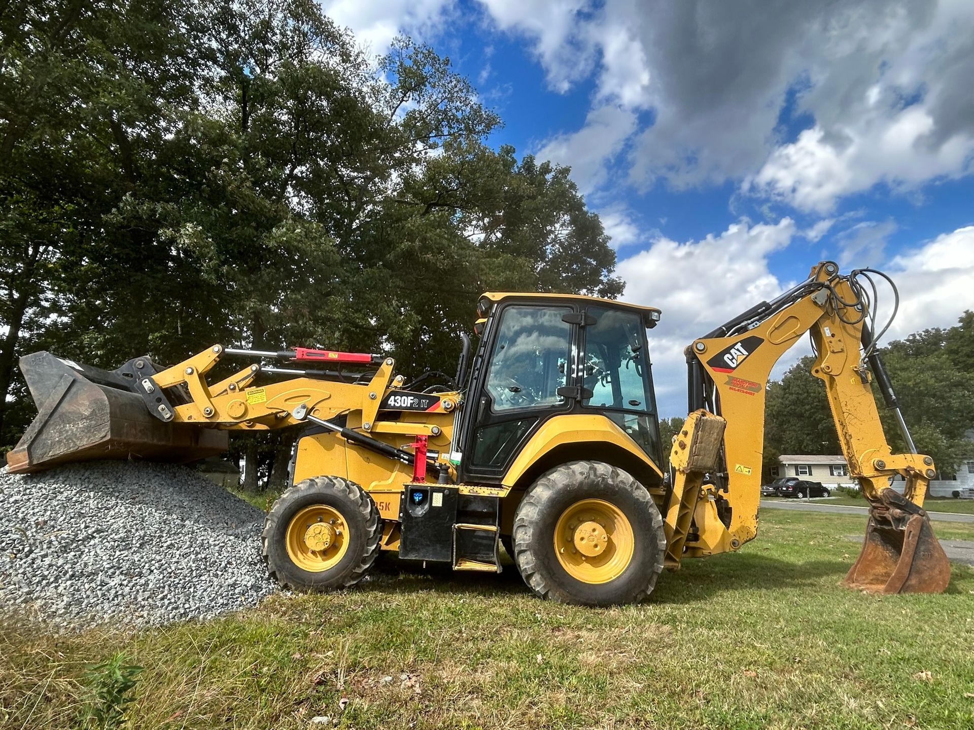 A yellow backhoe is sitting on top of a pile of gravel in a field.
