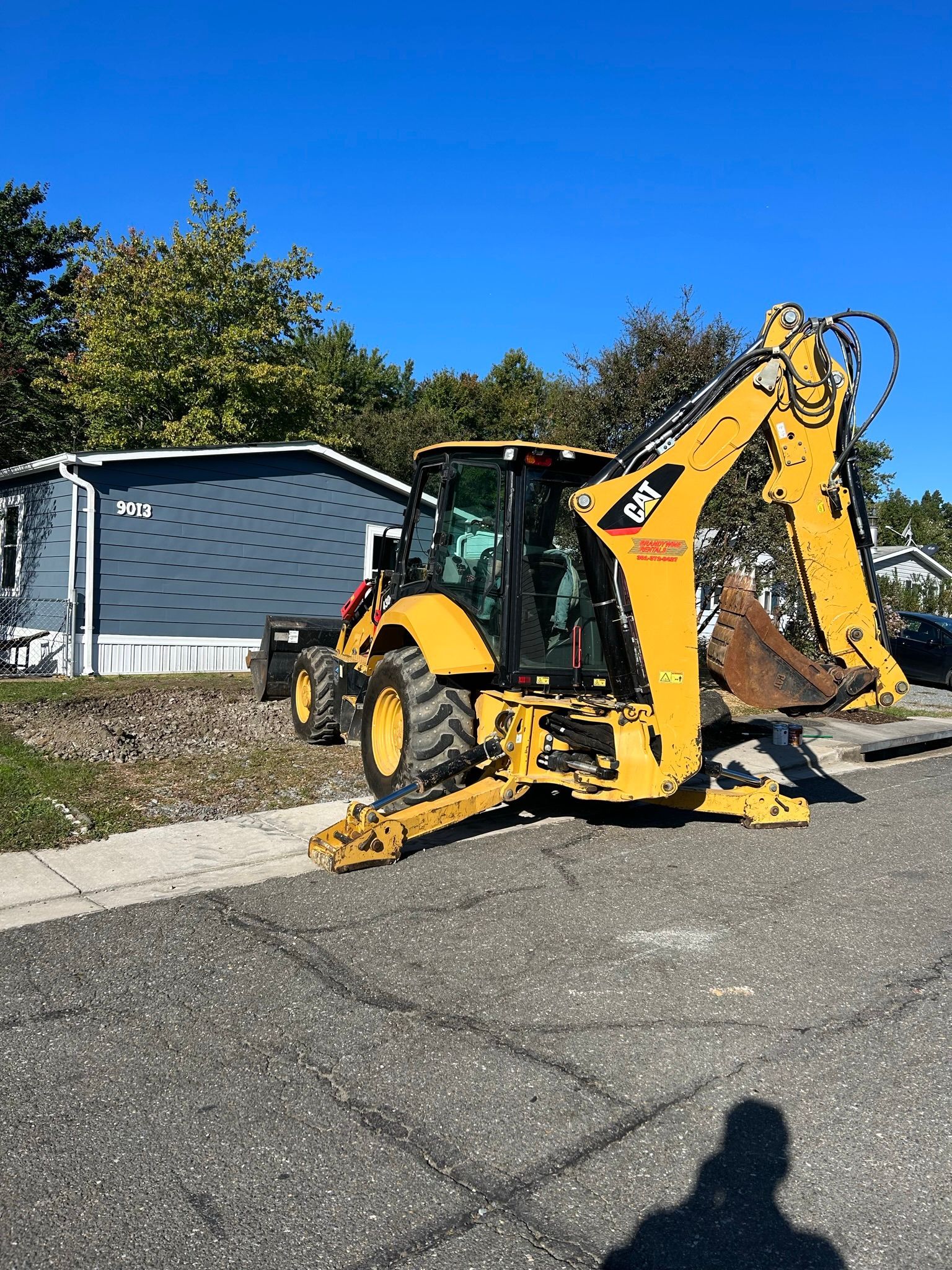 A yellow backhoe is parked on the side of the road in front of a house.