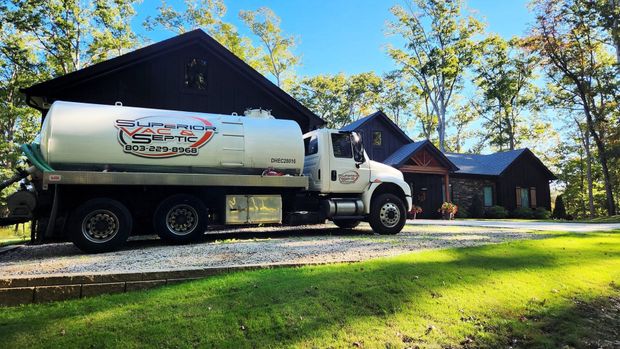 Orange tanker trailer parked on grass near a fence, with hoses attached at the rear