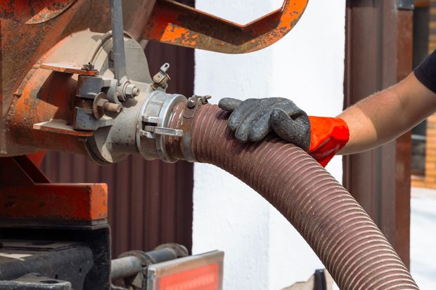 Gloved worker holding a corrugated hose attached to an industrial machine.