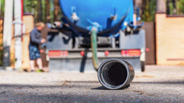 Black hose lying on pavement in front of a blue tanker truck being worked on outdoors Black hose lying on pavement in front of a blue tanker truck being worked on outdoors