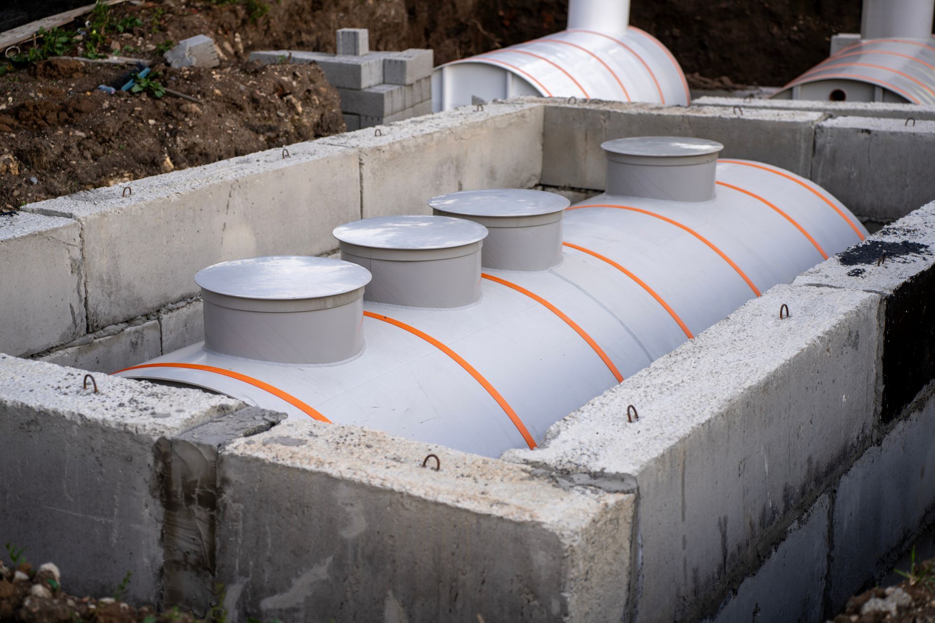 Cylindrical gray underground tank in a concrete pit, with orange bands and round access caps. Cylindrical gray underground tank in a concrete pit, with orange bands and round access caps.