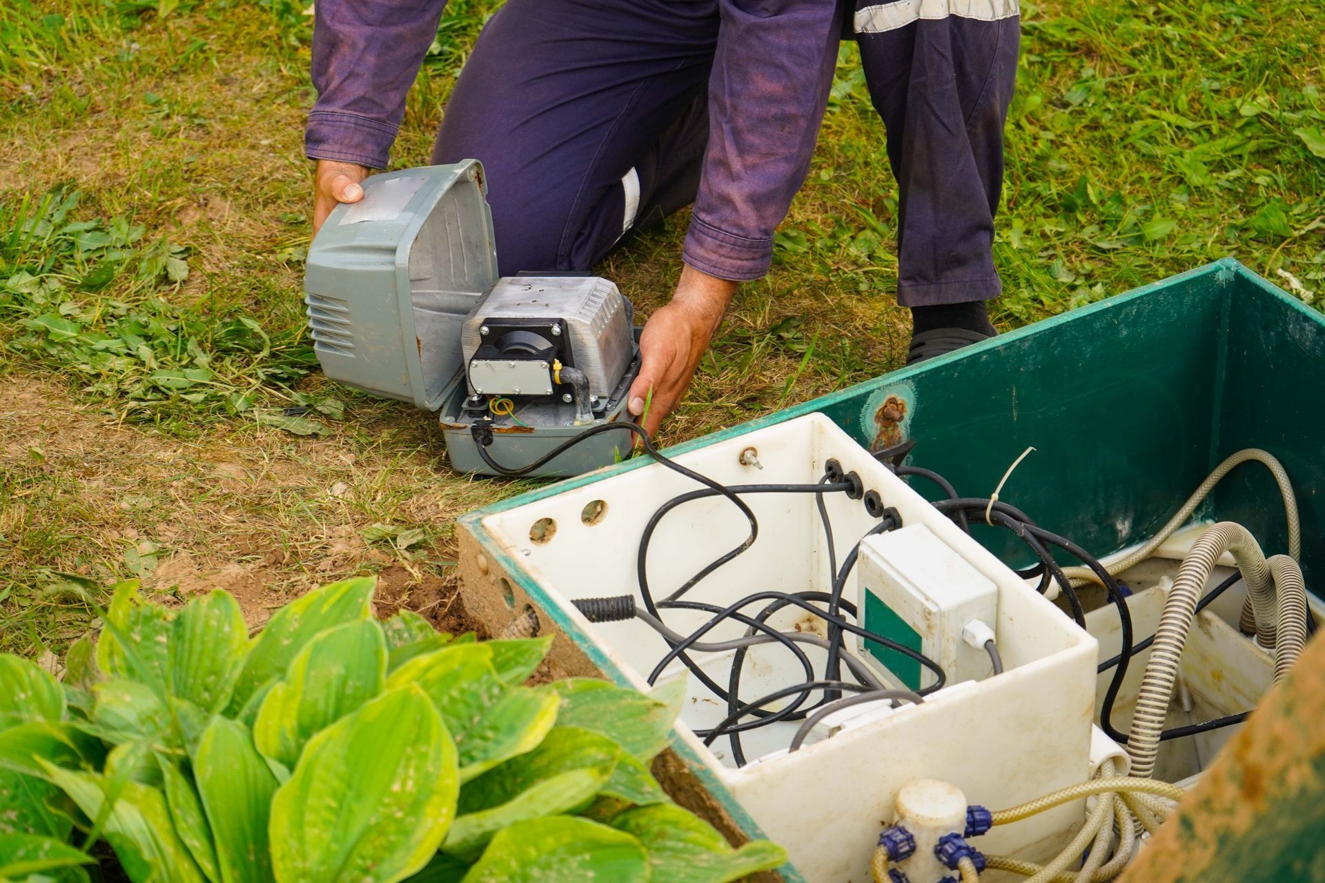 Person placing a gray machine beside a green utility box outdoors in a garden Person placing a gray machine beside a green utility box outdoors in a garden
