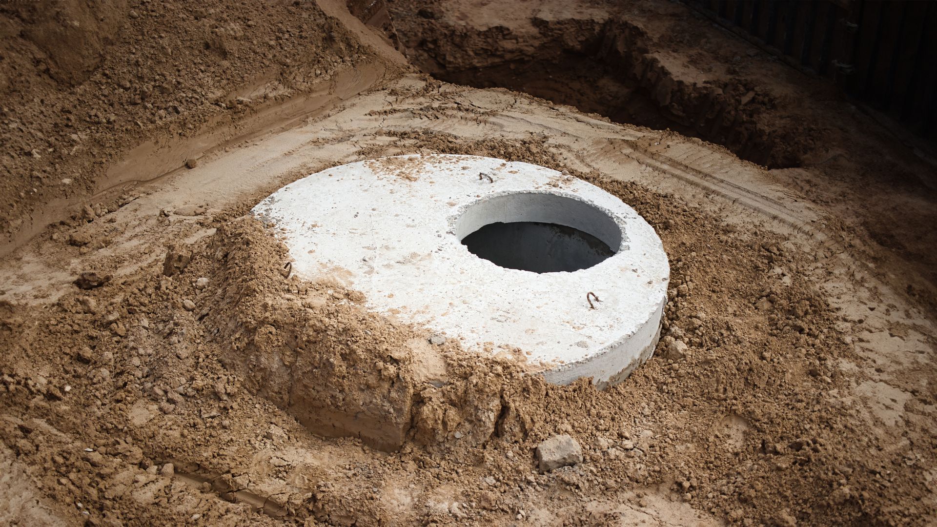 White circular concrete opening in a dirt pit, surrounded by excavated earth. White circular concrete opening in a dirt pit, surrounded by excavated earth.