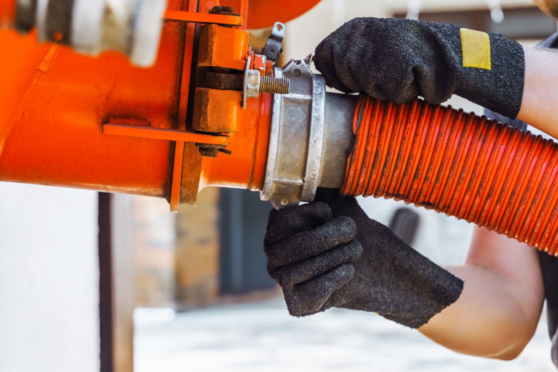 Gloved hands tightening a metal coupling on an orange industrial hose Gloved hands tightening a metal coupling on an orange industrial hose