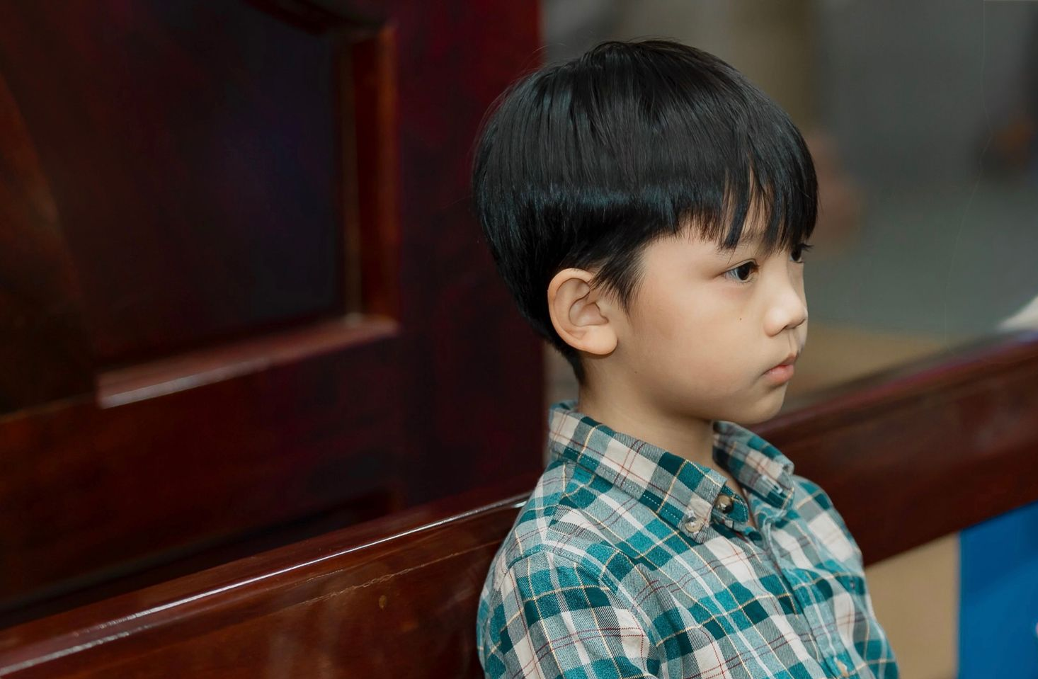 Young child in a plaid shirt looking to the right indoors