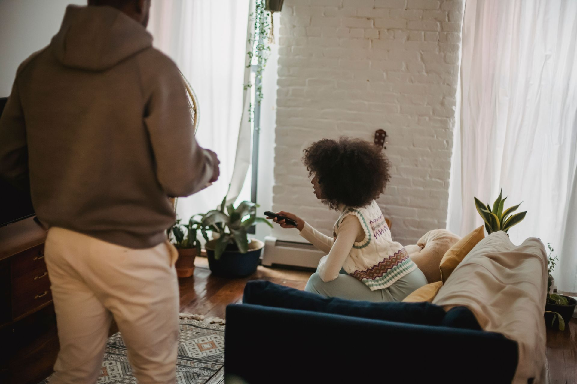 Person standing in a cozy living room while a child sits on a couch facing the window