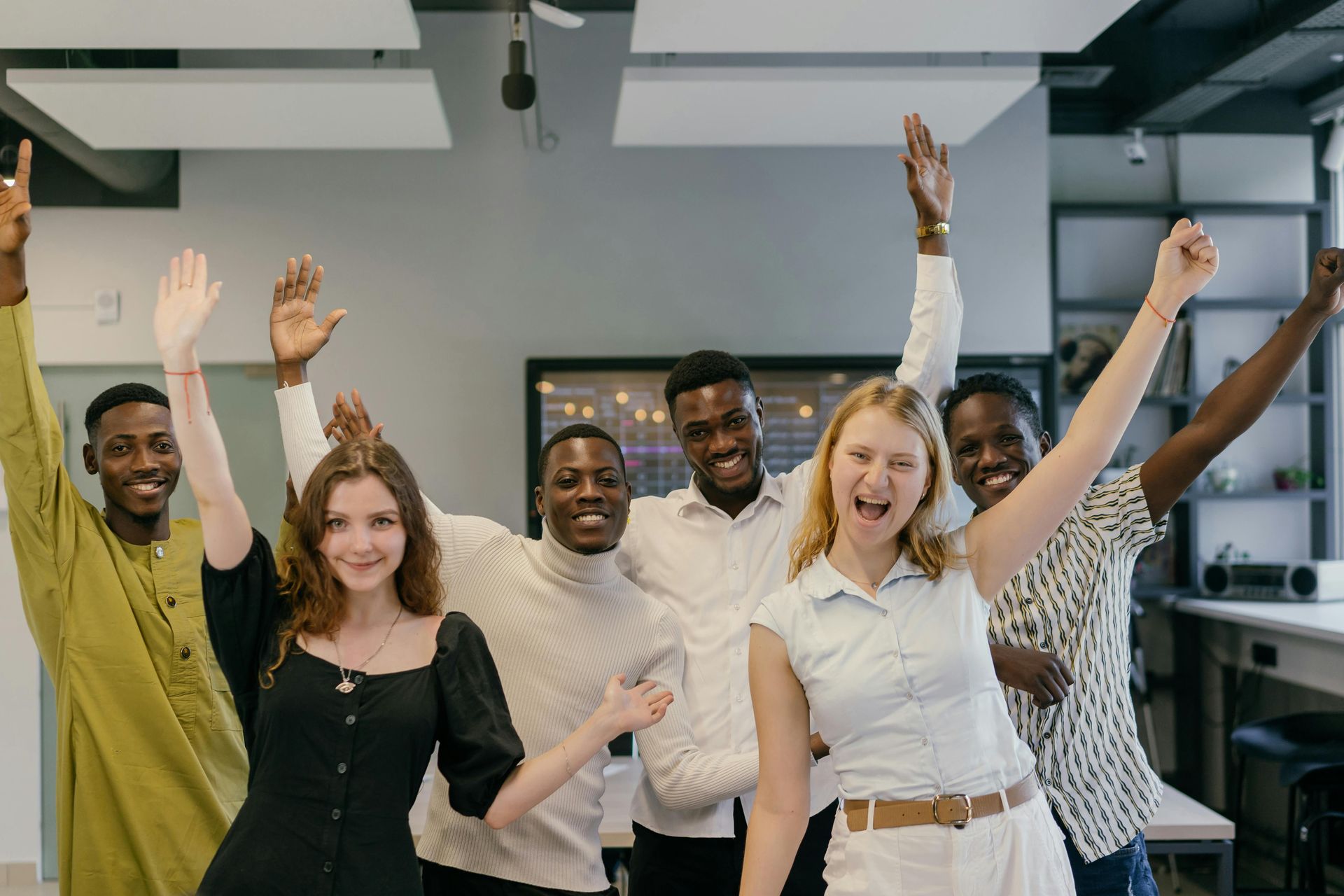Group of people celebrating in an office, raising arms and smiling.