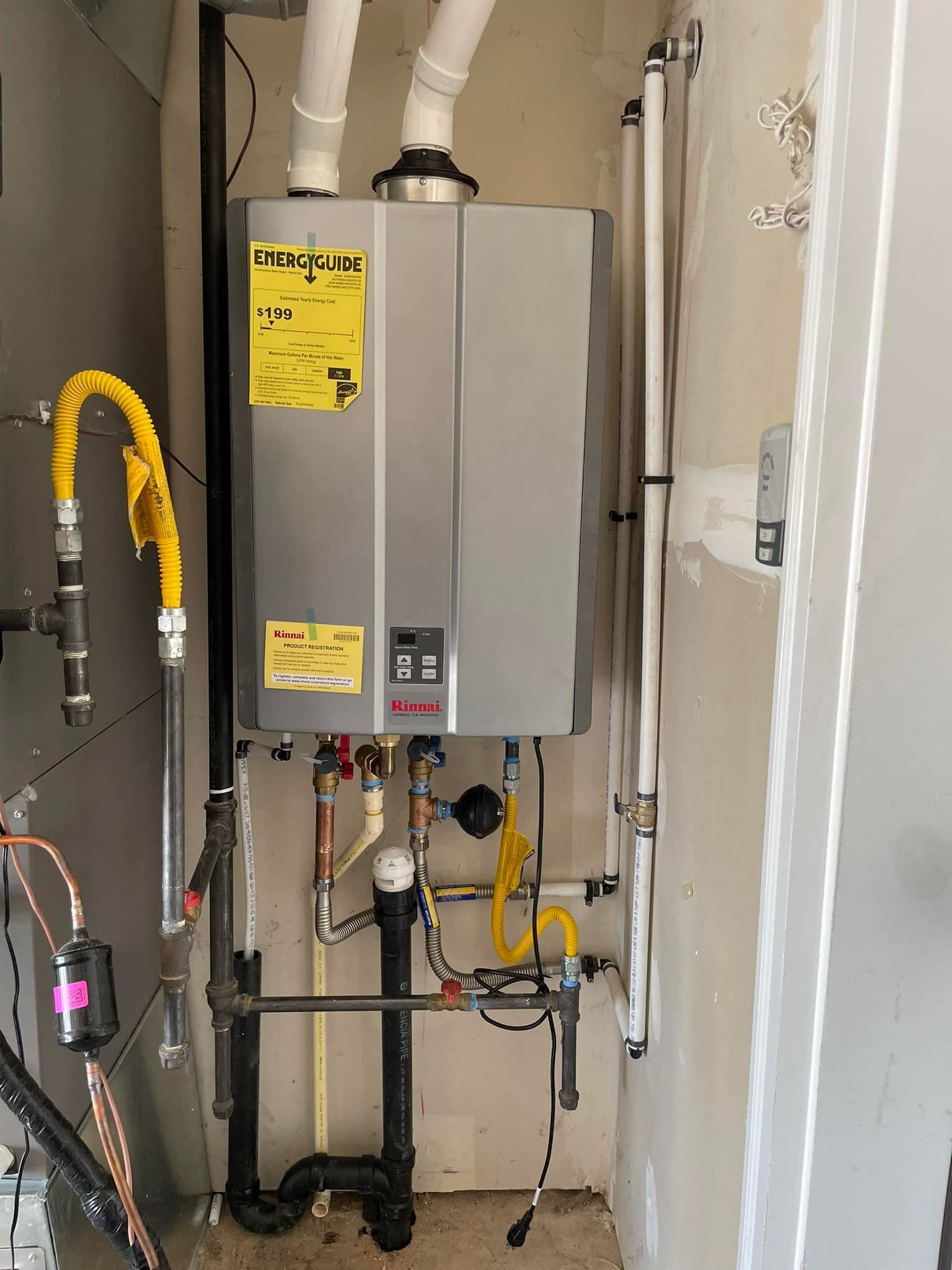 A tankless water heater installed in a utility closet with pipes and gas lines.